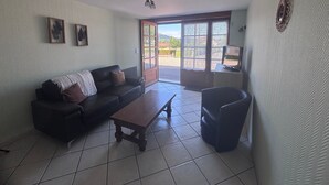 A living room with a sofa, a coffee table, a TV, and a door leading outside.