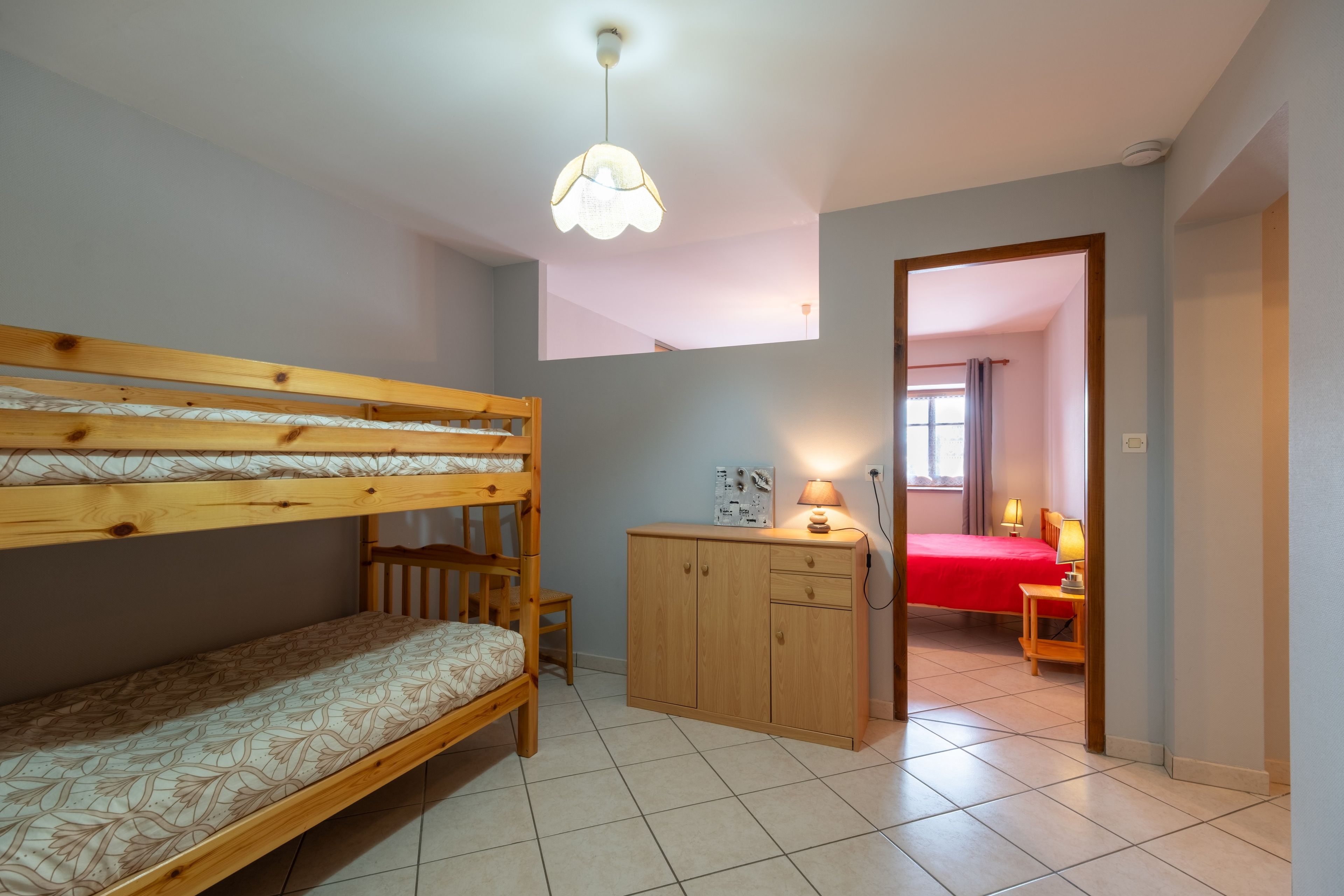 A room with bunk beds, a wooden cabinet, a desk, and a lamp.