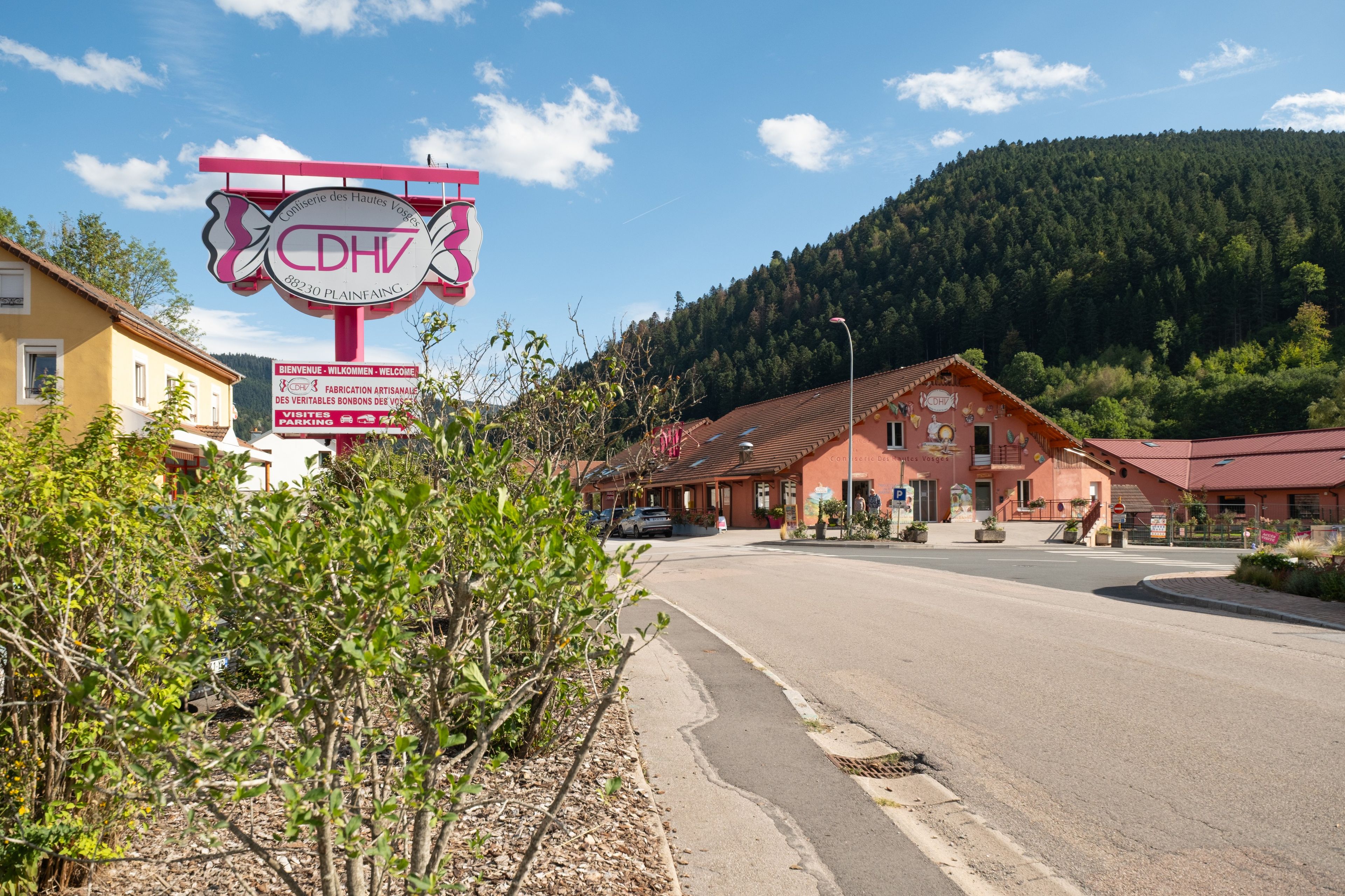 Señal de Conserverie des Hautes Vosges, un edificio con fachada roja y una carretera que lleva a él.
