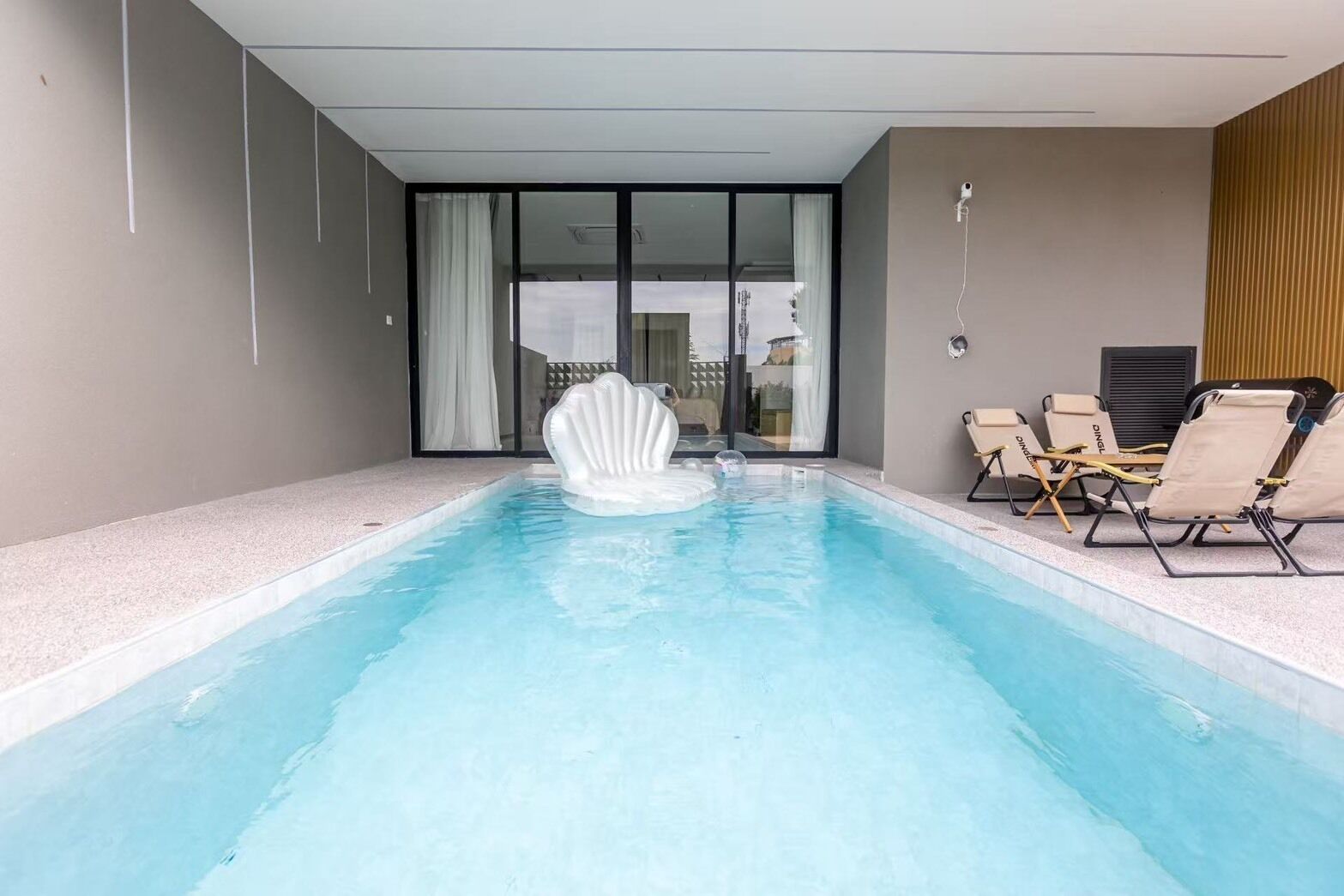 A swimming pool with a shell-shaped float, lounge chairs, and a sliding glass door leading to a balcony.