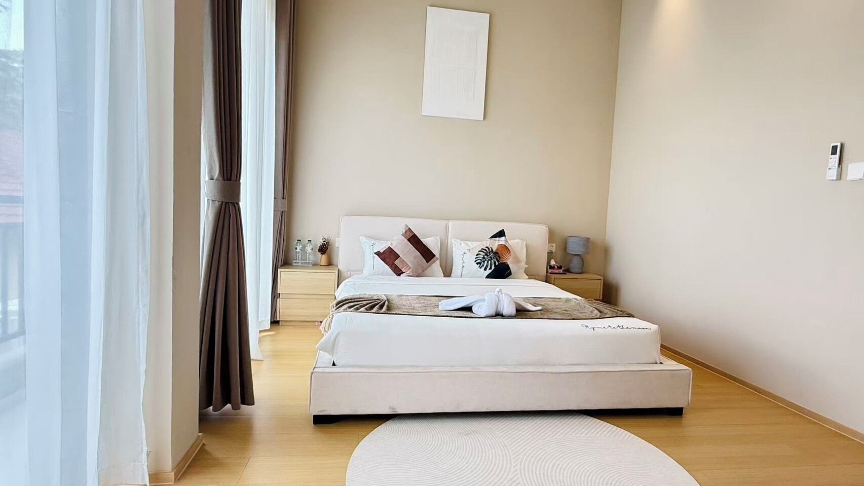 Habitación de hotel con cama, mesita de noche, lámpara y vistas al exterior.