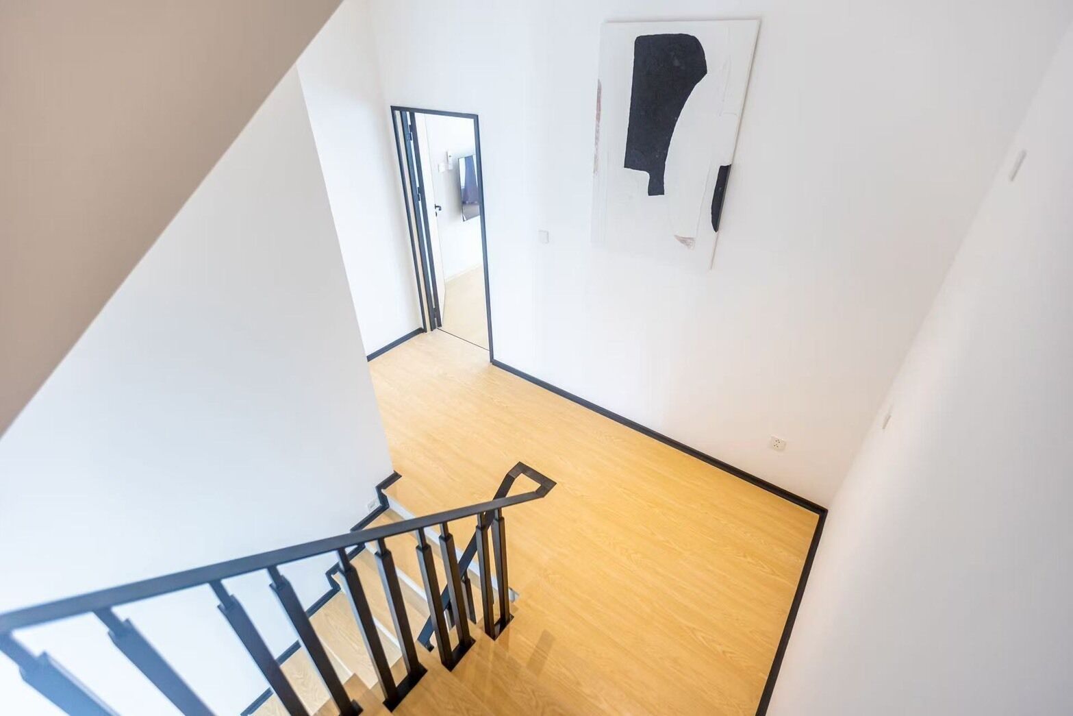 A staircase with a wooden floor and black railings leading to a room with white walls and a door.