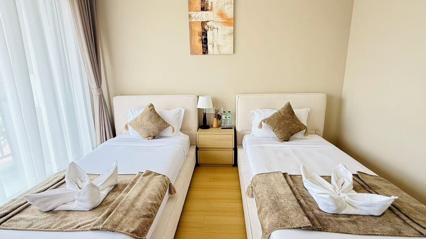 A hotel room with two beds, a nightstand with a lamp, and a painting on the wall.