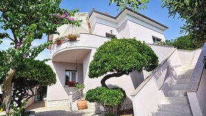 Ein modernes Haus mit einer geschwungenen Treppe, einem Balkon mit Blumentöpfen und einem gepflegten Garten.