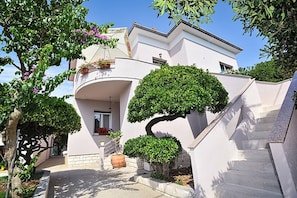 Ein modernes Haus mit einer geschwungenen Treppe, einem Balkon mit Blumentöpfen und einem gepflegten Garten.