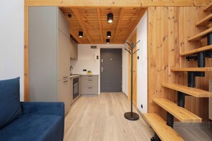 A compact kitchen with modern appliances, a dining area with a blue sofa, and a wooden staircase.