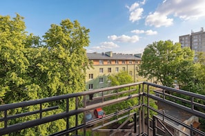 A residential building with multiple floors, a balcony, and a view of a tree-lined street.