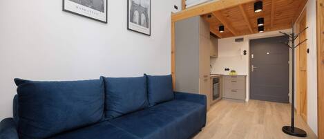 Una habitación moderna con un sofá azul, vigas de madera en el techo, una kitchenette y dos cuadros en la pared.