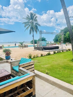 Een terras aan het strand met houten meubels, een palmboom en een podium.