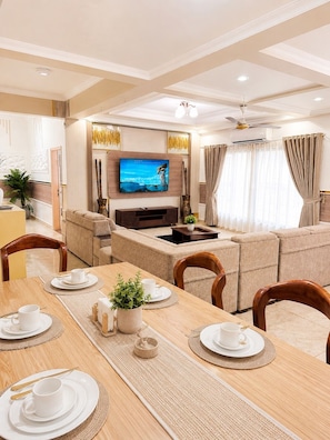 Een moderne woonkamer met een flatscreen-tv, een bank, een eettafel voor twee personen en een plafondventilator.