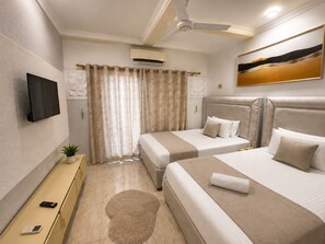 Een hotelkamer met twee bedden, een flatscreen televisie, een airconditioningapparaat, een plafondventilator en een schilderij aan de muur.