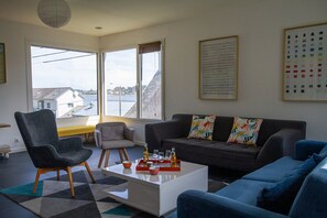 Ein modernes Wohnzimmer mit einer Couch, Sesseln, einem Couchtisch und Blick auf ein Gewässer durch große Fenster.