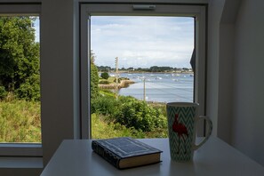 Ein Fenster mit Blick auf ein Gewässer, ein Buch und eine Tasse auf einem Tisch.
