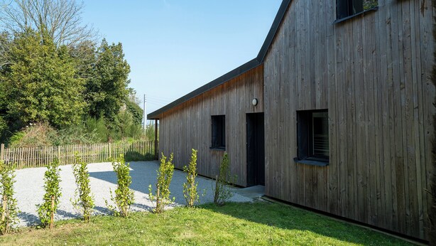 Un edifici modern de fusta amb teulada inclinada, un camí de grava i una tanca de fusta.