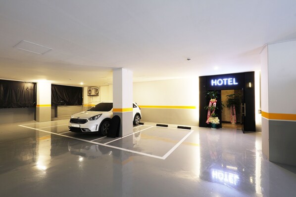 Zona de estacionamiento de un hotel, con un automóvil blanco aparcado, una entrada visible y un letrero que dice 'HOTEL'.