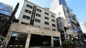 A hotel with a sign reading 'HOTEL STAY 25,' a parking garage entrance, and a tall building in the background. - Stay25 (Seongnam)