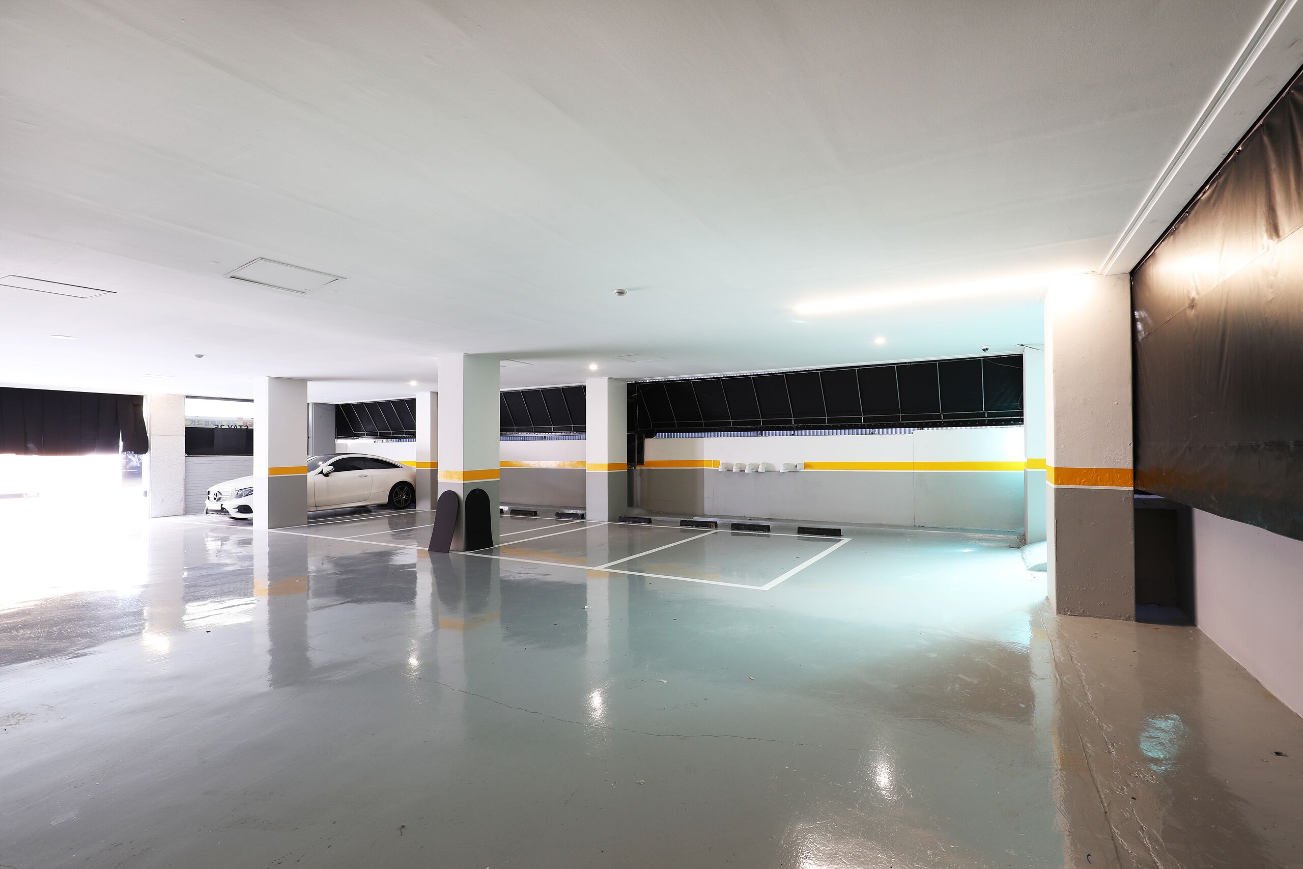 A parking garage with white walls, yellow and black striped columns, and a white car parked in the distance.