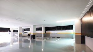 A parking garage with white walls, yellow and black striped columns, and a white car parked in the distance. - Stay25 (Seongnam)
