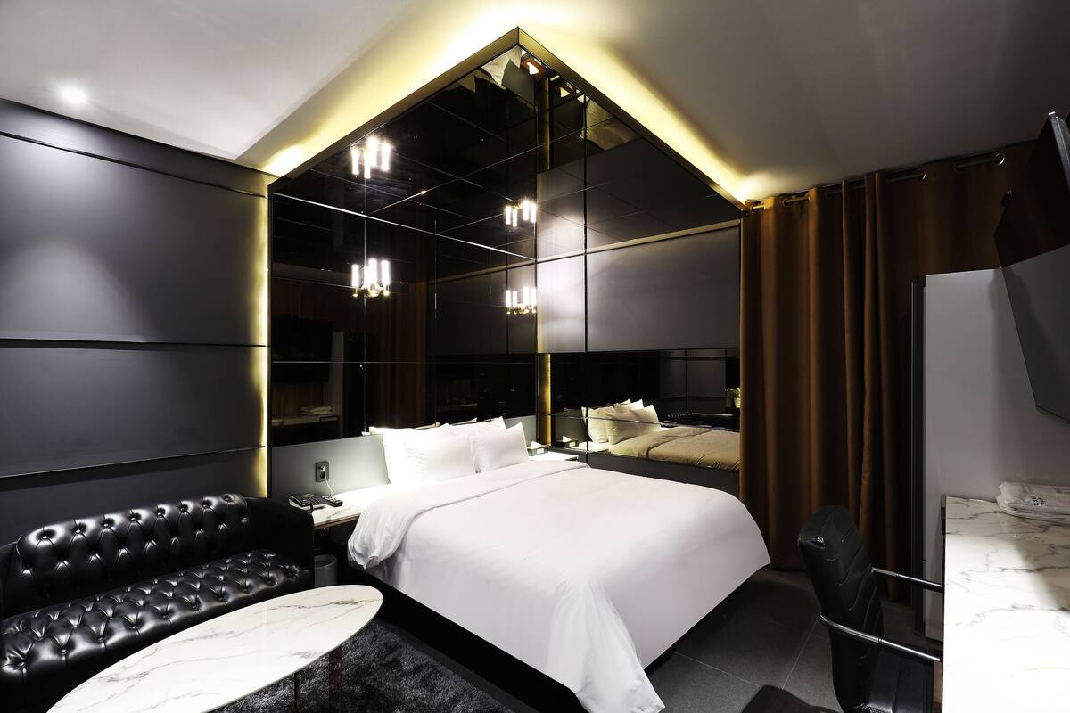 Una habitación de hotel moderna con una cama grande, un sofá de cuero negro, una mesa con cubierta de mármol y un espejo grande.