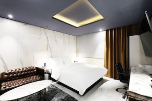 Una habitación de hotel moderna con una cama grande, un sofá de cuero, una mesita redonda y un escritorio con una silla.