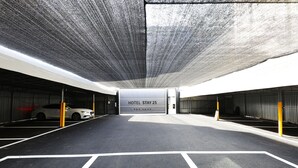 A hotel parking garage with a white car parked, a sign reading 'HOTEL STAY 25', and yellow bollards. - Stay25 (Seongnam)