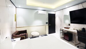 A modern hotel room with a bed, a seating area, a desk, a television, and an air conditioning unit. - Stay25 (Seongnam)
