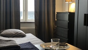 Habitación de hotel con una cama, una mesita de noche con un vaso de agua, una lámpara y vistas al exterior.