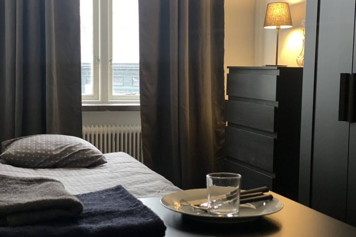 A hotel room with a bed, a bedside table with a glass of water, a lamp, and a view of the outside.