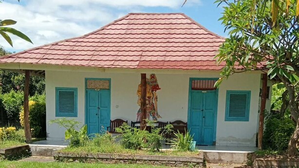 A single-story building with a red-tiled roof, a small porch, and a grassy yard. - Hepi Bungalow Lovina Bali (Buleleng)