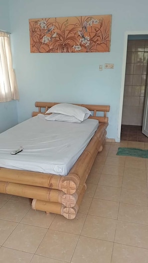 Una habitación con cama, un cuadro en la pared, una ventana con cortinas y suelo de baldosas.