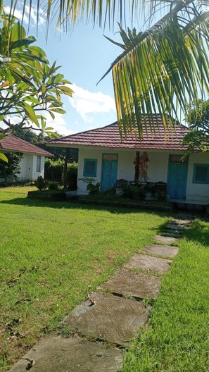A house with a tiled roof, a front porch, and a grassy yard. - Hepi Bungalow Lovina Bali (Buleleng)