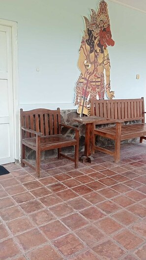 A room with a tiled floor, two wooden benches, and a wall with a large decorative painting. - Hepi Bungalow Lovina Bali (Buleleng)