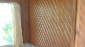 A room with a wooden floor, a dark wooden bench, a window with curtains, and a textured wall. - Hepi Bungalow Lovina Bali (Buleleng)