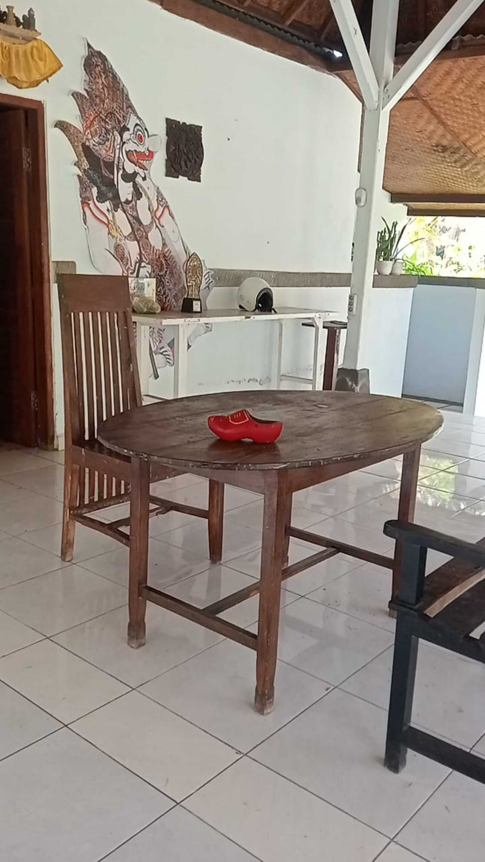 Una mesa de madera con un objeto rojo encima, una silla y una pared con un mural.