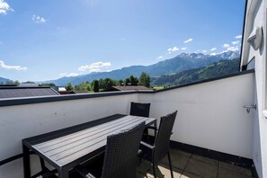 Un balcón con mesa y sillas, vistas a montañas y una pared blanca.