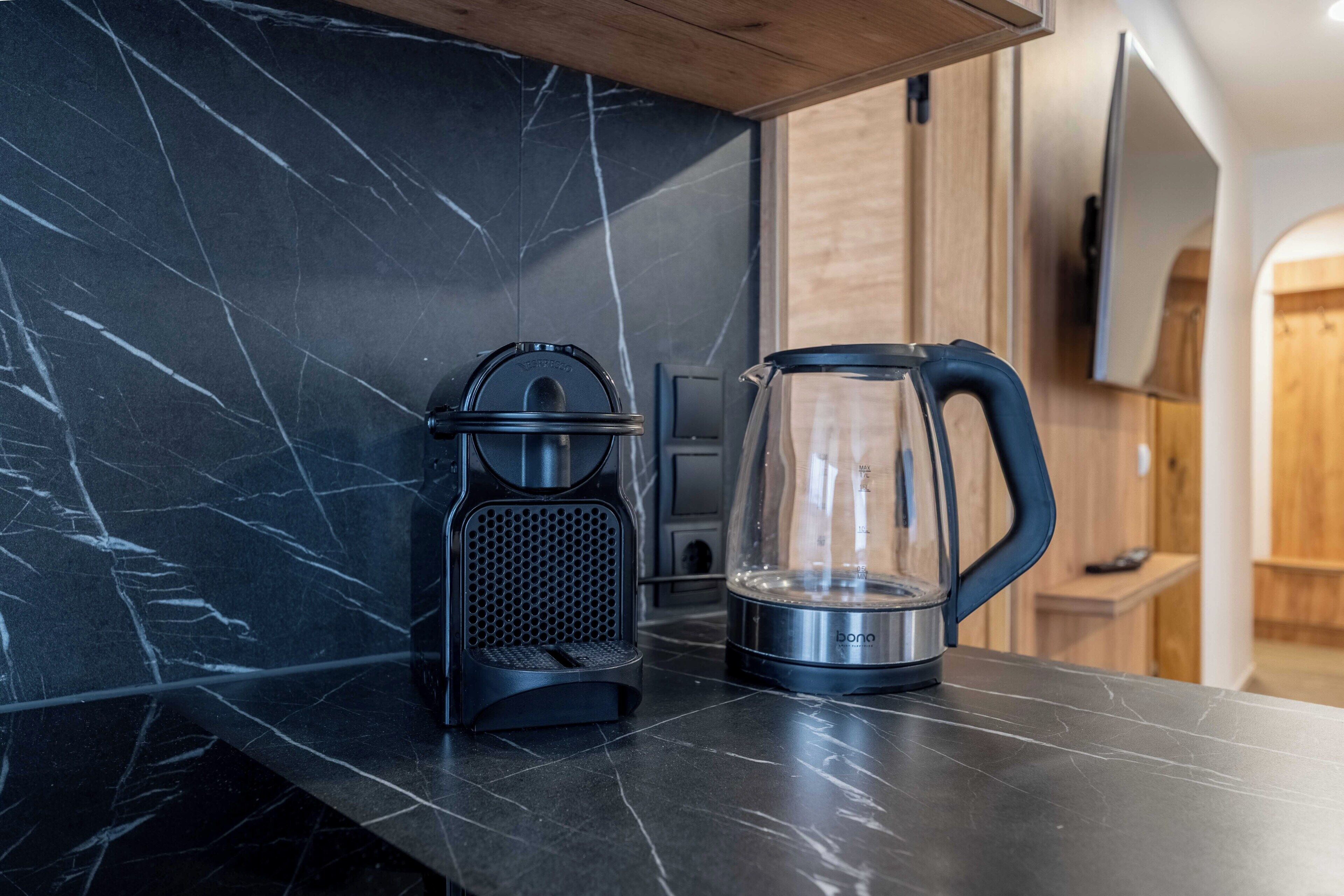 Een keuken met een marmeren aanrecht, een koffiezetapparaat en een glazen waterkoker.