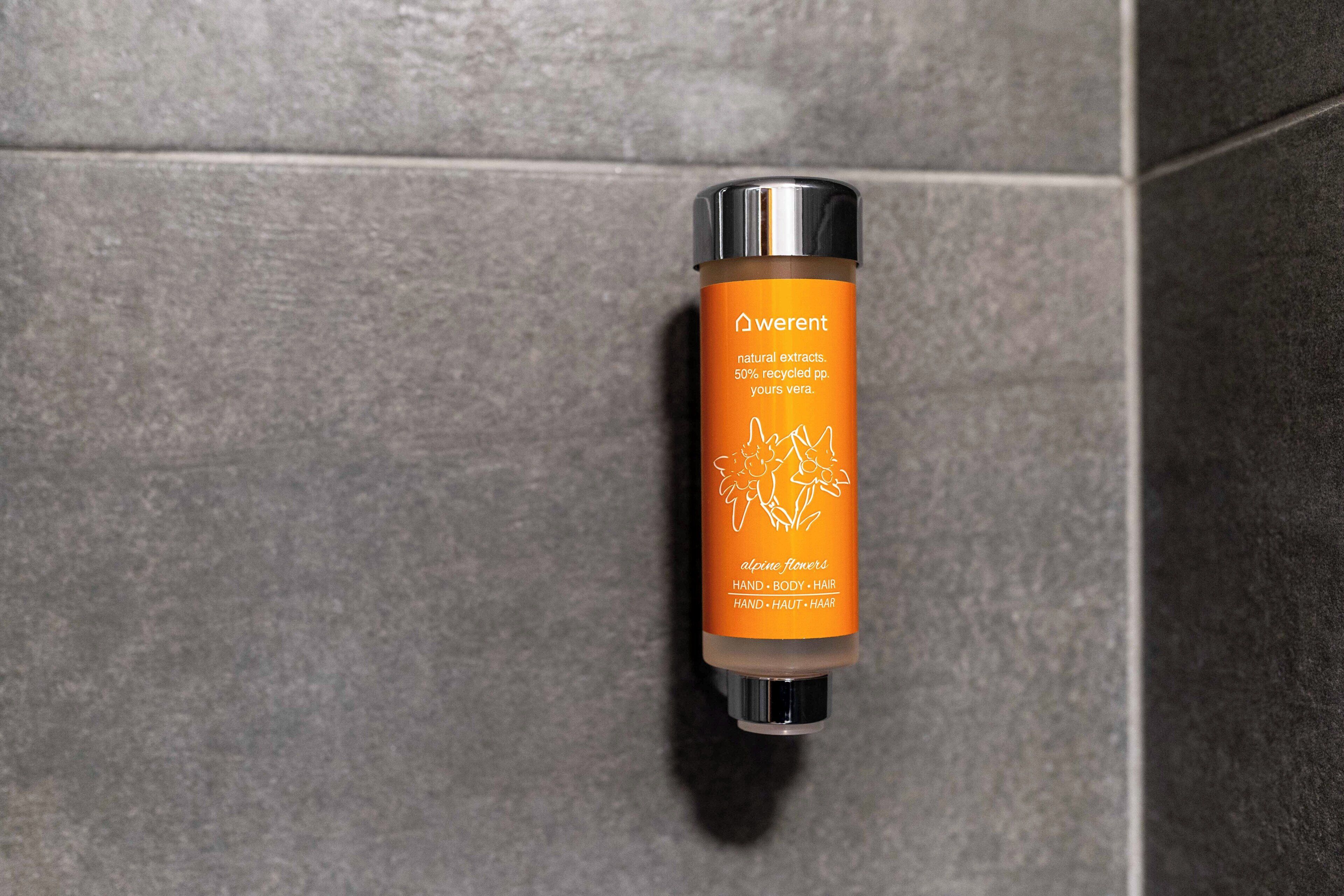 A bottle of Weren't natural extracts hand, body, and hair product against a tiled wall.