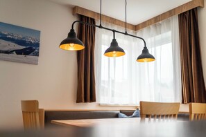 Uma sala de jantar com uma mesa e cadeiras de madeira, um banco e um quadro com paisagem nevada de montanhas.