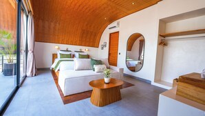 Ein modernes Hotelzimmer mit einem großen Bett, einem runden Holztisch, einem großen Spiegel und Blick ins Freie.