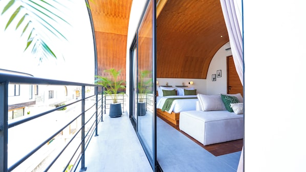 A balcony with a metal railing, a bed with white bedding and green pillows, and a potted plant. - K Club Cemagi Villa 5 (Badung)