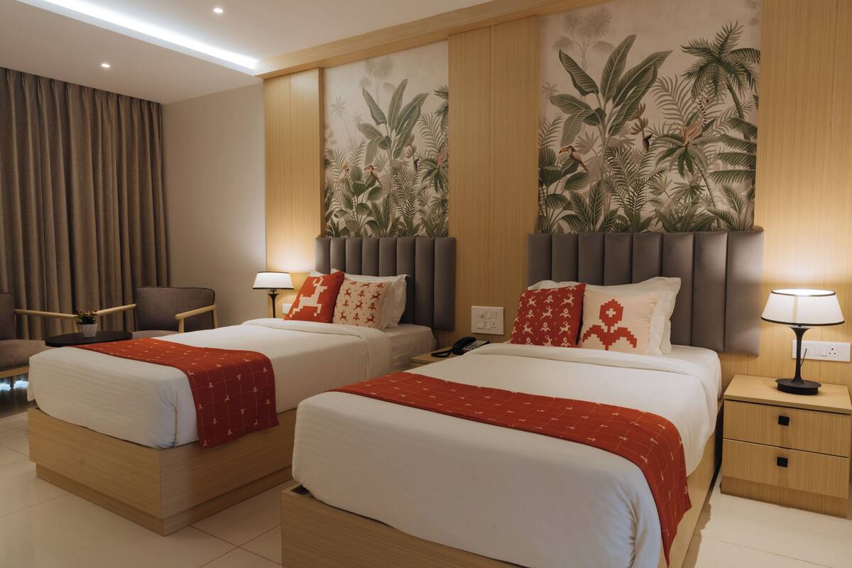 A hotel room with two beds, a desk, a chair, a nightstand, and a wall with a tropical mural.
