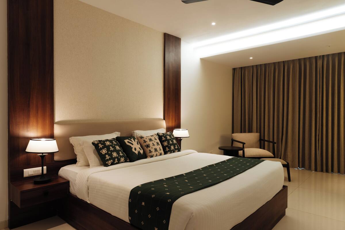 A hotel room with a large bed, two bedside tables with lamps, a chair, and a view of the outside through curtains.