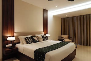 A hotel room with a large bed, two bedside tables with lamps, a chair, and a view of the outside through curtains.