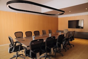 A conference room with a long table, black chairs, a flat-screen TV, and wooden panel walls.