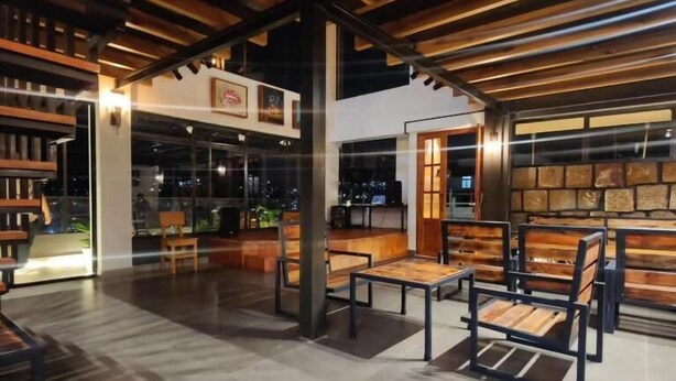 An indoor seating area with wooden benches and tables, a stone wall, and a view of the outside. - Cafe Sola bnb (Shillong)