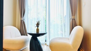 Quarto com duas cadeiras brancas, uma mesa redonda com um vaso e cortinas leves.