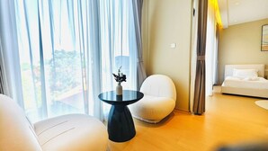 Quarto de hotel moderno com uma mesa redonda preta, uma poltrona branca, um sofá e uma cama com roupa de cama branca.