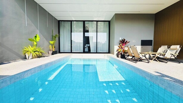 Piscina com bordas azulejadas, área de espreguiçadeiras e plantas em vasos.