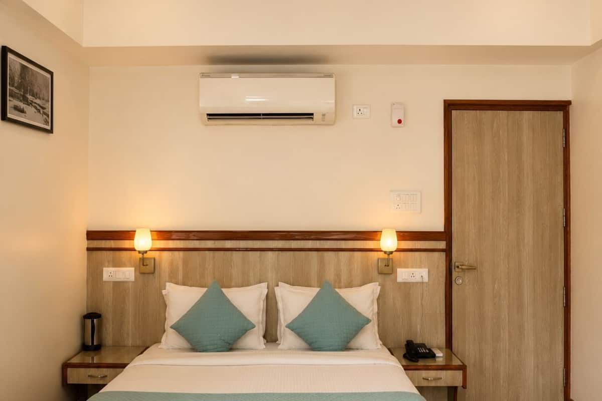 Habitación de hotel con cama, mesitas de noche, ventilador de techo, aire acondicionado y puerta de madera.