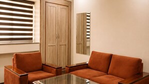Un salon avec une table basse en verre, deux canapés, un parquet, une fenêtre avec des stores et une armoire en bois.